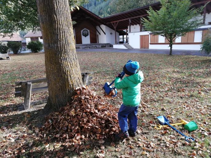 Kind von hinten, steht mit Schaufel bei einem Blätterhaufen