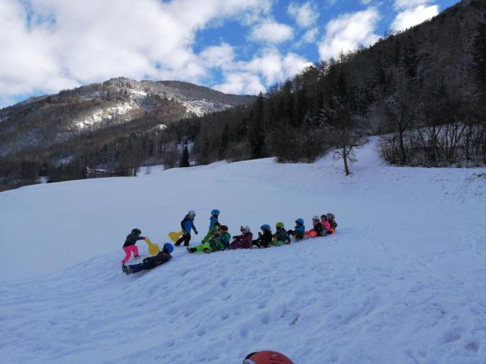 Kinder sitzen hintereinander auf Rutschtellern im Schnee